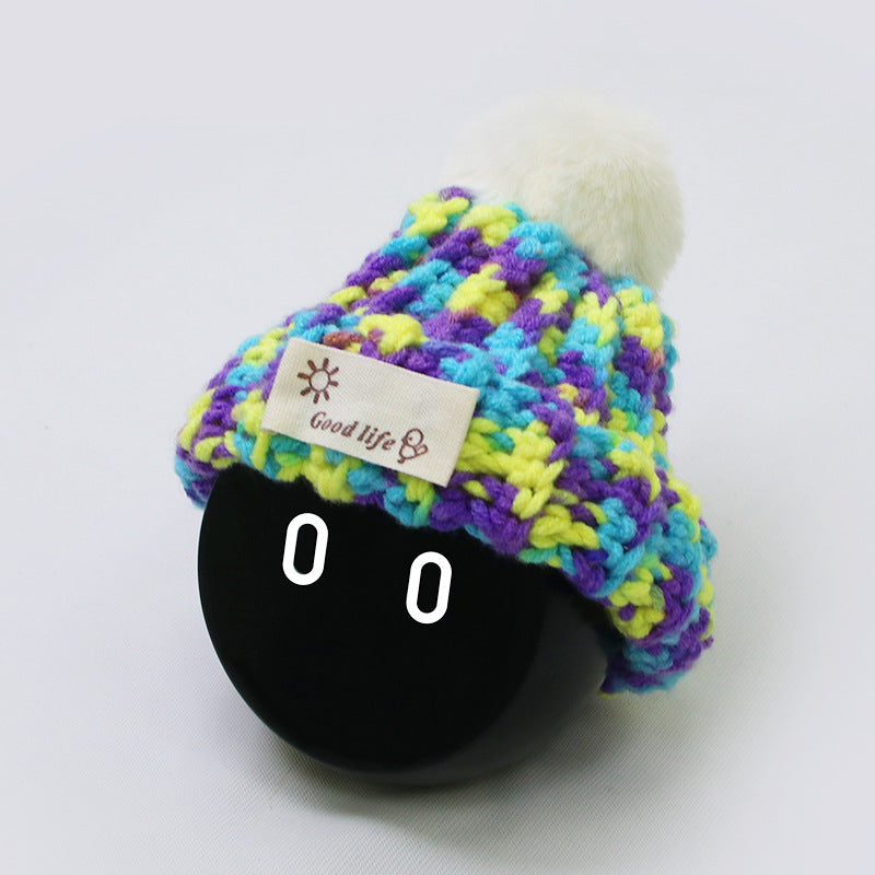 The Mixed PB beanie is knitted from a mix of purple, yellow, and blue yarns and has a white ball on top.